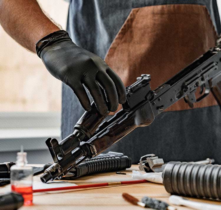 Freedom Firearms & Defense | Person wearing gloves working on a disassembled firearm on a workbench.