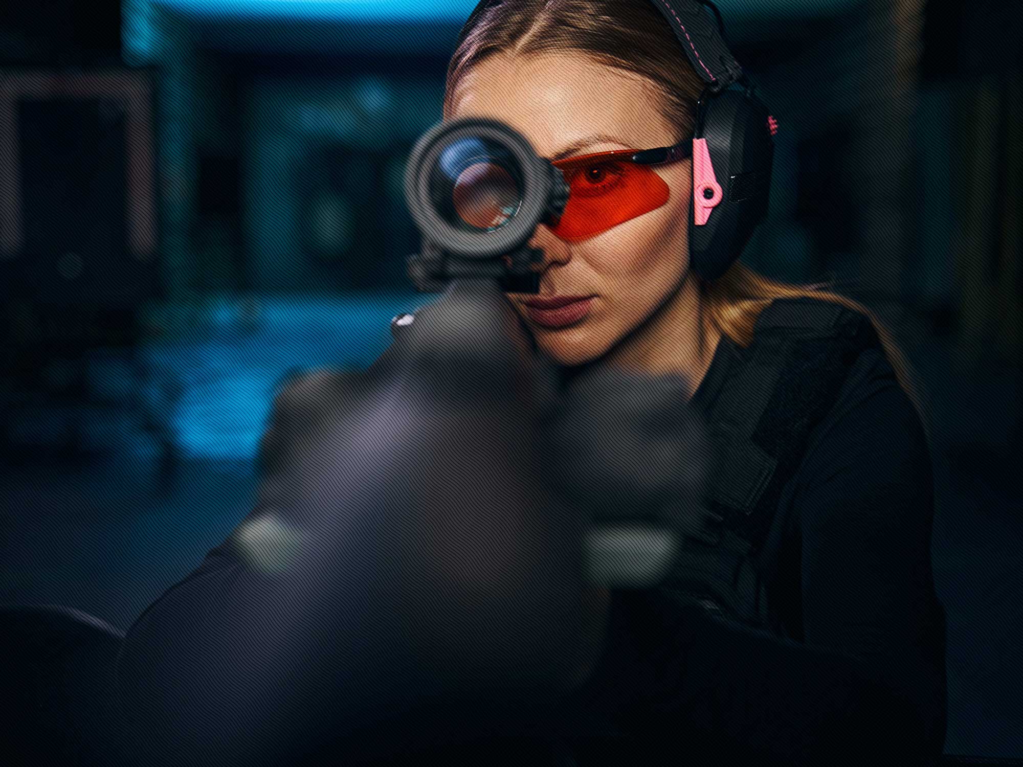 Freedom Firearms & Defense | Woman aiming a firearm with a scope, wearing protective headphones and eyewear.