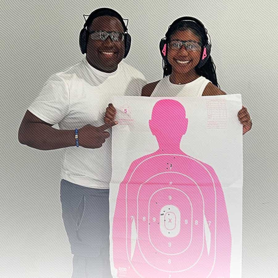 Freedom Firearms & Defense | Two people wearing safety gear are holding a target practice sheet with bullet holes. They are smiling and appear to be at a shooting range.